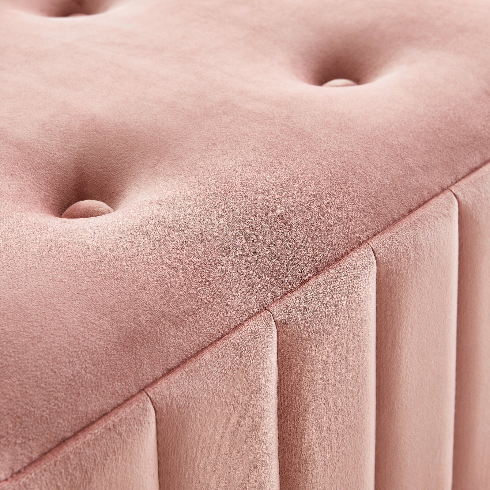 Nahaufnahme einer rosa gepolsterten Hockerbank mit Knopfdetails und vertikalen Nähten, perspektivisch von oben fotografiert.