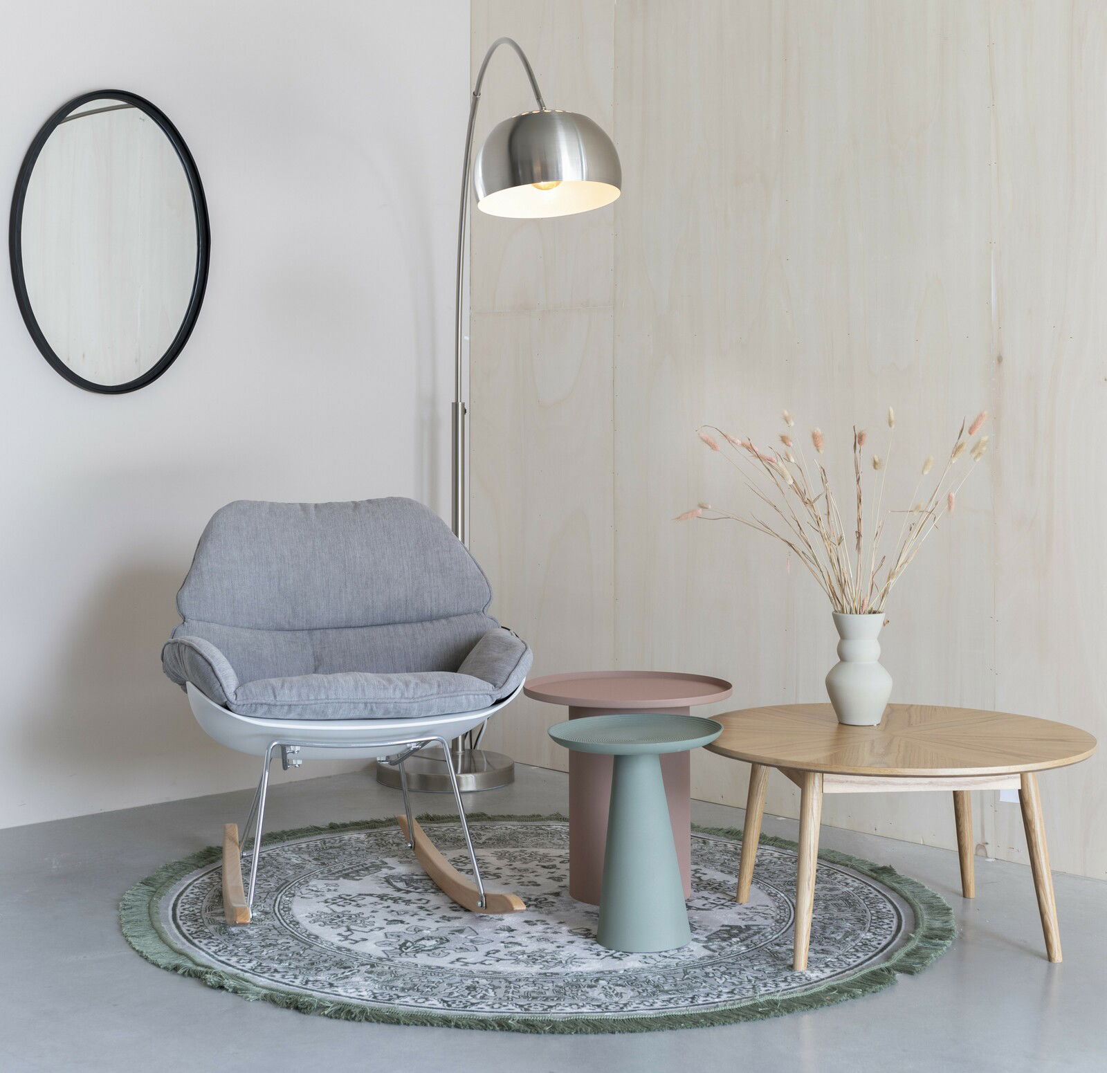 Moderner Schaukelsessel in Grau, umgeben von einem eleganten Wohnzimmer-Setup mit Beistelltischen und Stehlampe, seitliche Perspektive.