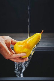 Close-up van een hand die een peer onder stromend water houdt, met de focus op de waterstraal.