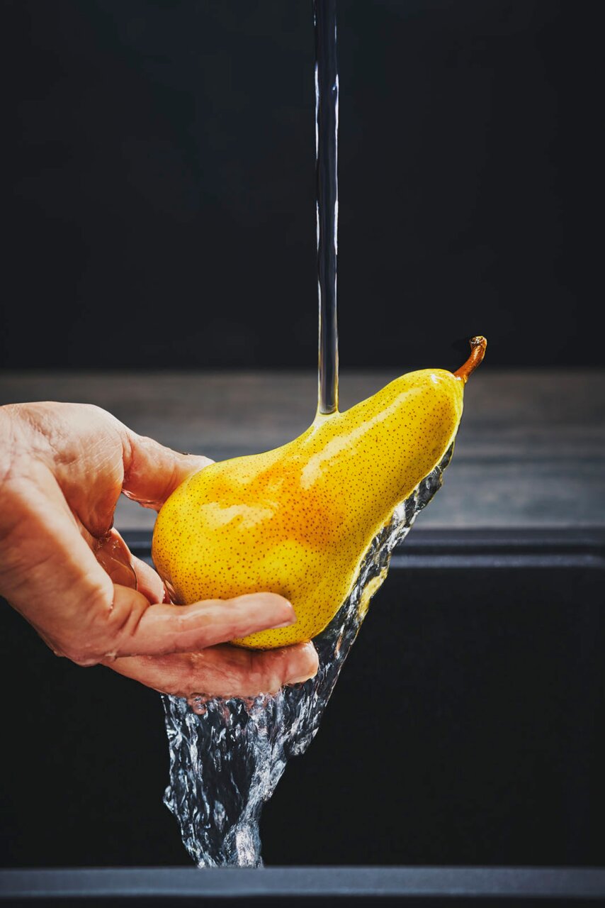 Close-up van een hand die een peer onder stromend water houdt, met de focus op de waterstraal.