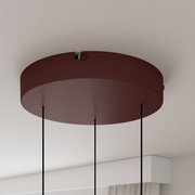 Runde Deckenhalterung einer Pendelleuchte in Bordeauxrot mit drei schwarzen Abhängeseilen, aus Untersicht/leicht schräg von unten fotografiert.