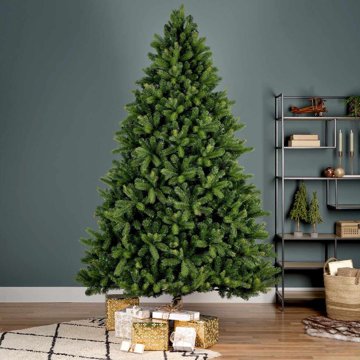 Everlands Künstliche Kiefertanne FREIBURG 180cm Künstlicher Weihnachtsbaum in einem Wohnzimmer, frontal fotografiert, mit Geschenken darunter und einem Regal im Hintergrund.
