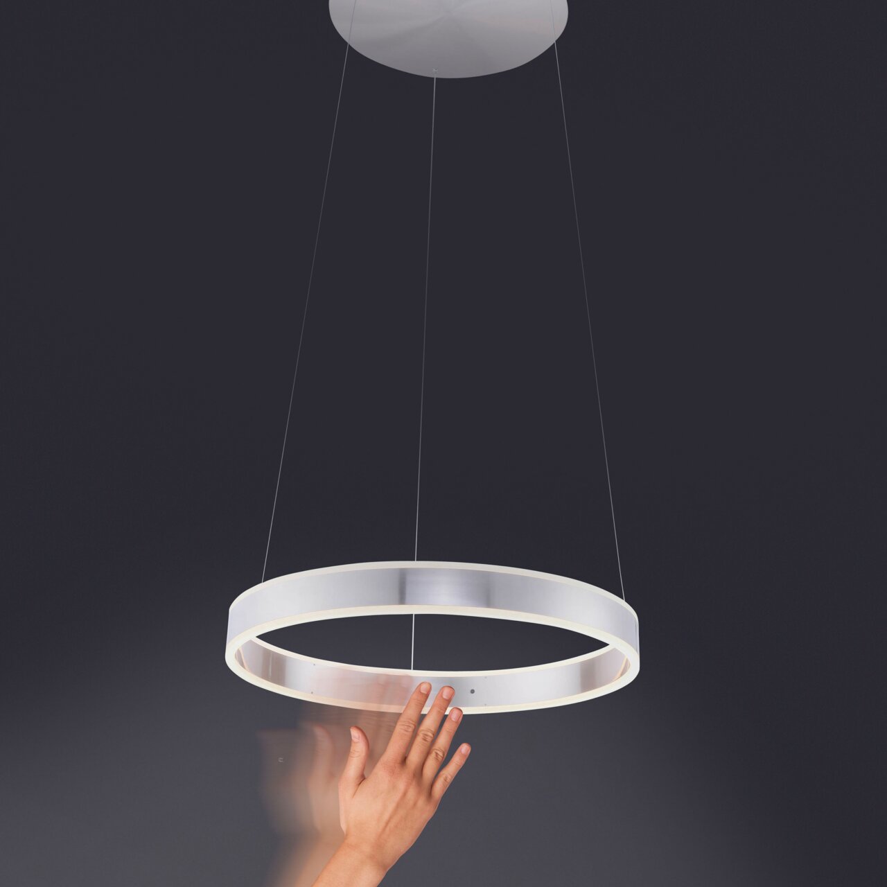 Moderne hanglamp in de vorm van een ring, gezien van onderaf, met een hand die de kap aanraakt.