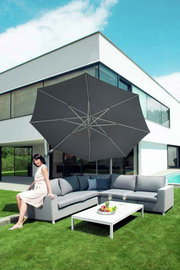 Moderner Pendelschirm über einer eleganten Outdoor-Sitzgruppe mit einer Frau, die auf dem Sofa sitzt, vor einem modernen Haus. Perspektive von schräg vorne.