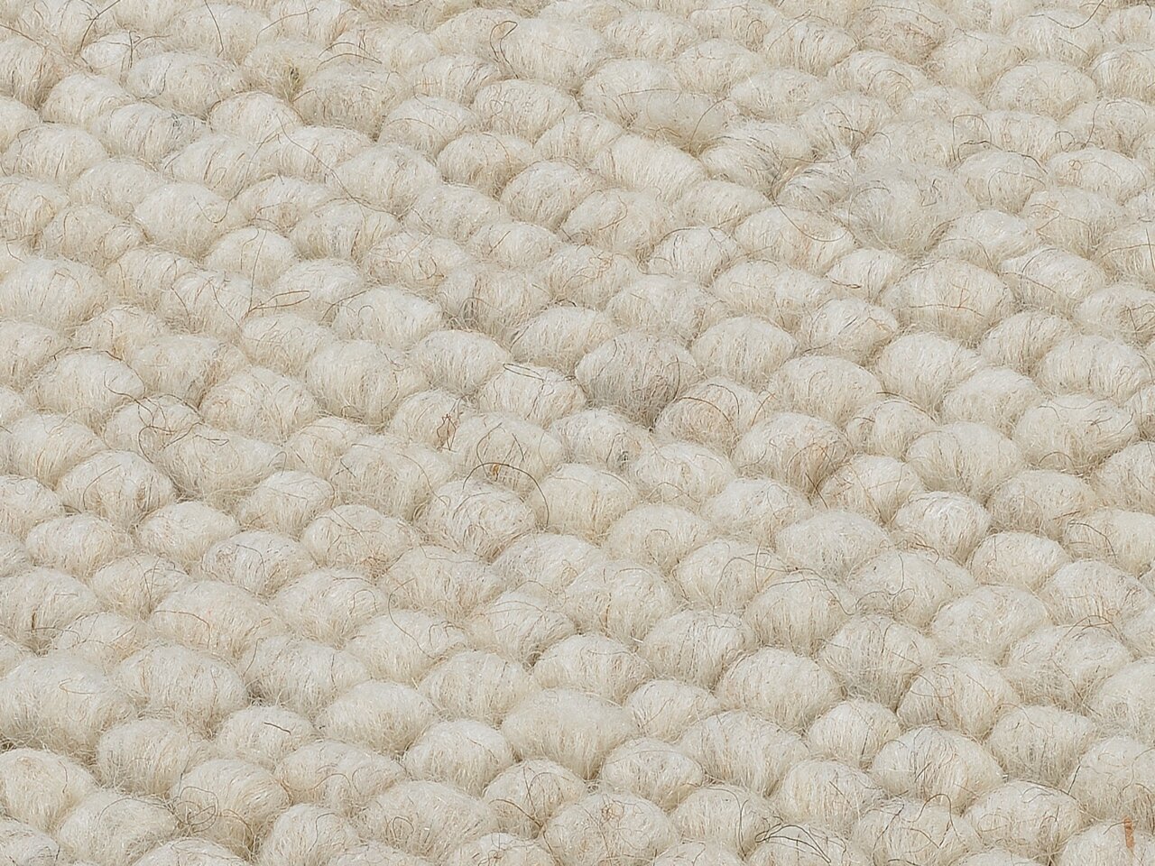 Nahaufnahme eines handgewebten Teppichs mit einer strukturierten, wolligen Oberfläche in cremeweißer Farbe.