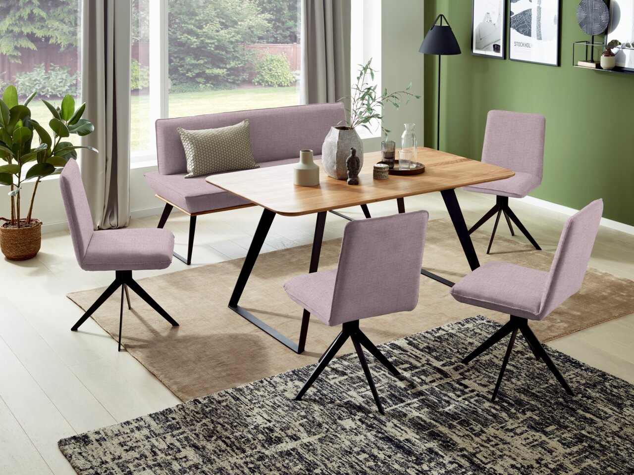 Esszimmer mit moderner Bank und Stühlen in lila Stoffbezug, Holztisch und grüner Wand im Hintergrund, seitliche Perspektive