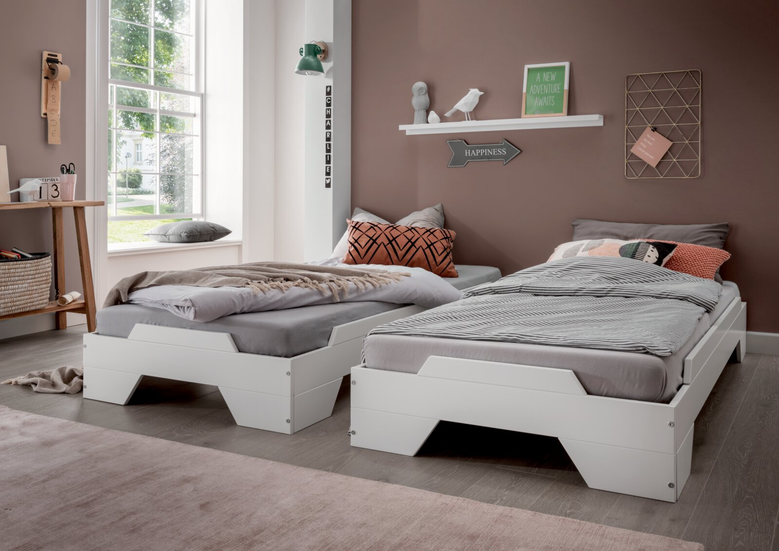 Zwei weiße Stapelbetten in einem modernen Schlafzimmer mit großen Fenstern, seitliche Perspektive