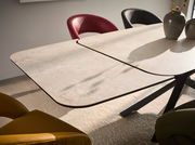 Moderner Esstisch mit heller Tischplatte und schwarzem Gestell, umgeben von bunten Stühlen, aus seitlicher Perspektive fotografiert.