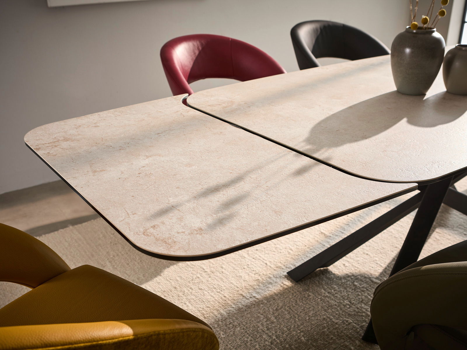 Moderner Esstisch mit heller Tischplatte und schwarzem Gestell, umgeben von bunten Stühlen, aus seitlicher Perspektive fotografiert.