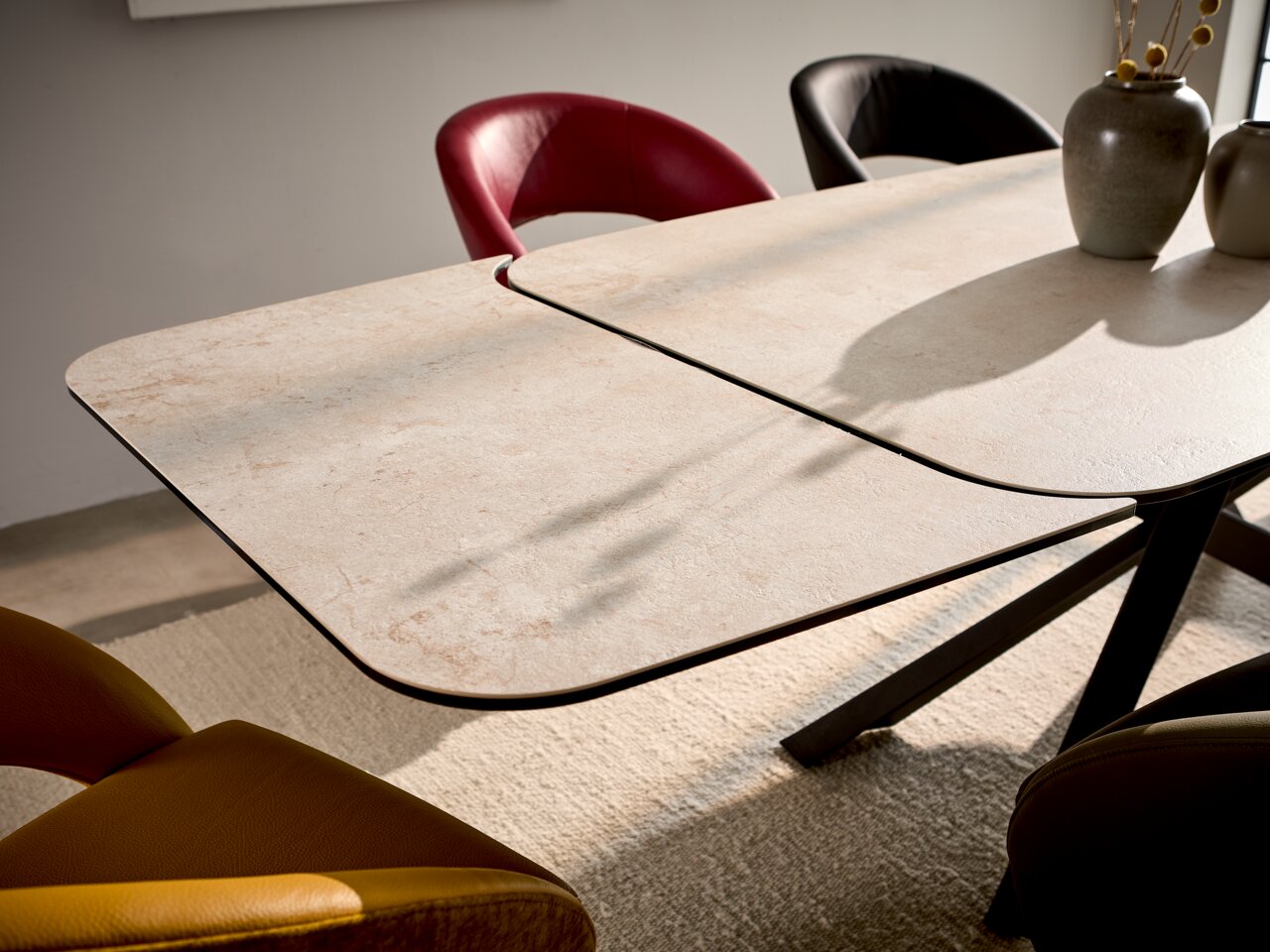 Moderne eettafel met een lichtgekleurd tafelblad en een zwart onderstel, omringd door kleurrijke stoelen, gefotografeerd vanuit een zijaanzicht.