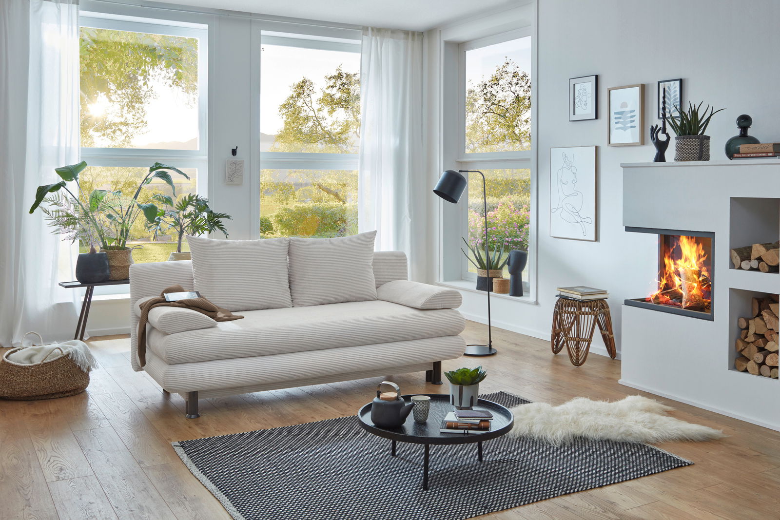 Modernes Funktionssofa in einem hellen Wohnzimmer mit großen Fenstern, Pflanzen und einem Kamin, seitliche Perspektive.