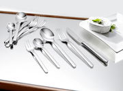 Elegantes 60-teiliges Besteckset aus Edelstahl, von oben betrachtet, auf einem glänzenden Tisch neben einem Teller mit Käse.