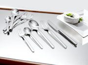 Elegantes 60-teiliges Besteckset aus Edelstahl, von oben betrachtet, auf einem glänzenden Tisch neben einem Teller mit Käse.