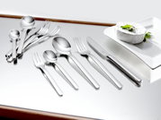 Elegantes 60-teiliges Besteckset aus Edelstahl, von oben betrachtet, auf einem glänzenden Tisch neben einem Teller mit Käse.
