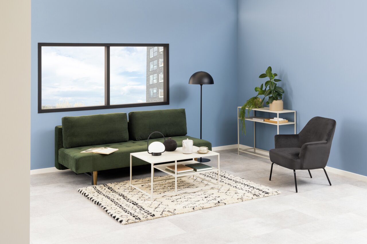 Grünes Funktionssofa in modernem Wohnzimmer mit blauer Wand, schwarzem Sessel und Beistelltisch, seitliche Perspektive.