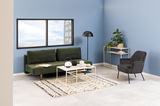 Grünes Funktionssofa in modernem Wohnzimmer mit blauer Wand, schwarzem Sessel und Beistelltisch, seitliche Perspektive.