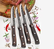 Vier Steakmesser HUNTER mit gehämmerten Klingen und Holzgriffen, von oben fotografiert, auf einem Schneidebrett mit Gewürzen und Chili.