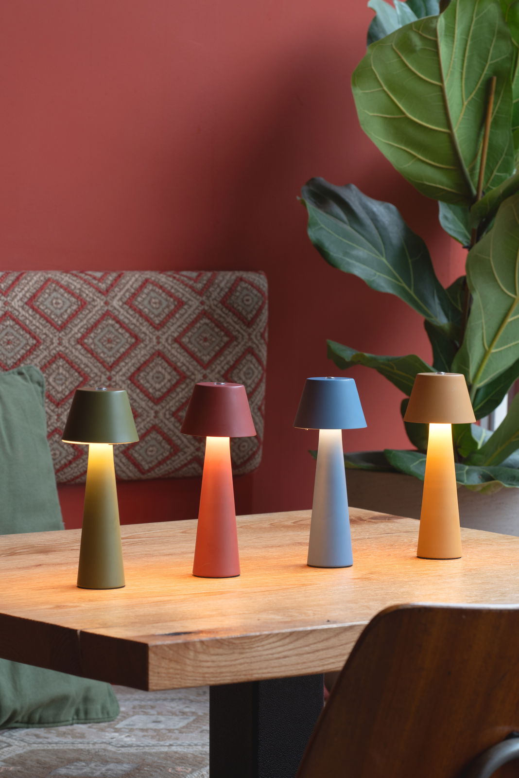 Vier bunte LED Akku Tischleuchten in verschiedenen Farben (Grün, Rot, Blau, Gelb) auf einem Holztisch, seitliche Perspektive.