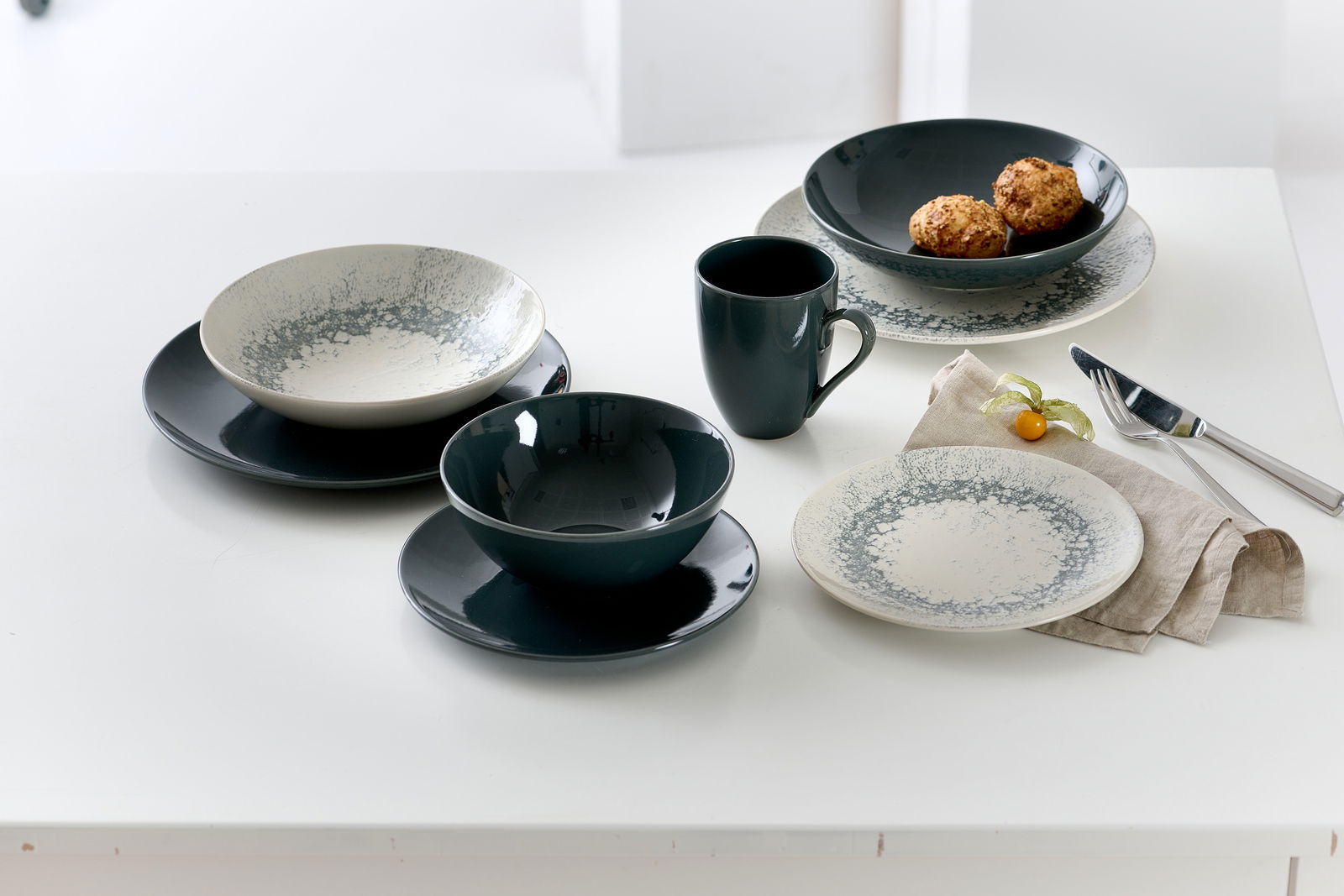 Vogelperspektive auf ein stilvolles Geschirrset mit grauen und cremefarbenen Speisetellern, Schalen und einer Tasse auf einem weißen Tisch.