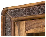 Detailansicht einer Vitrine mit kunstvoll geschnitztem Holzrahmen und dekorativen Metallverzierungen.