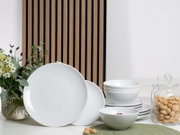 Weißes Porzellan-Geschirrset mit großen Tellern, Schalen und kleinen Tellern auf einem Tisch arrangiert, frontal in leichter Seitenansicht fotografiert; daneben Glasdose mit Keksen und Blumenvase vor Holzlamellen-Hintergrund.