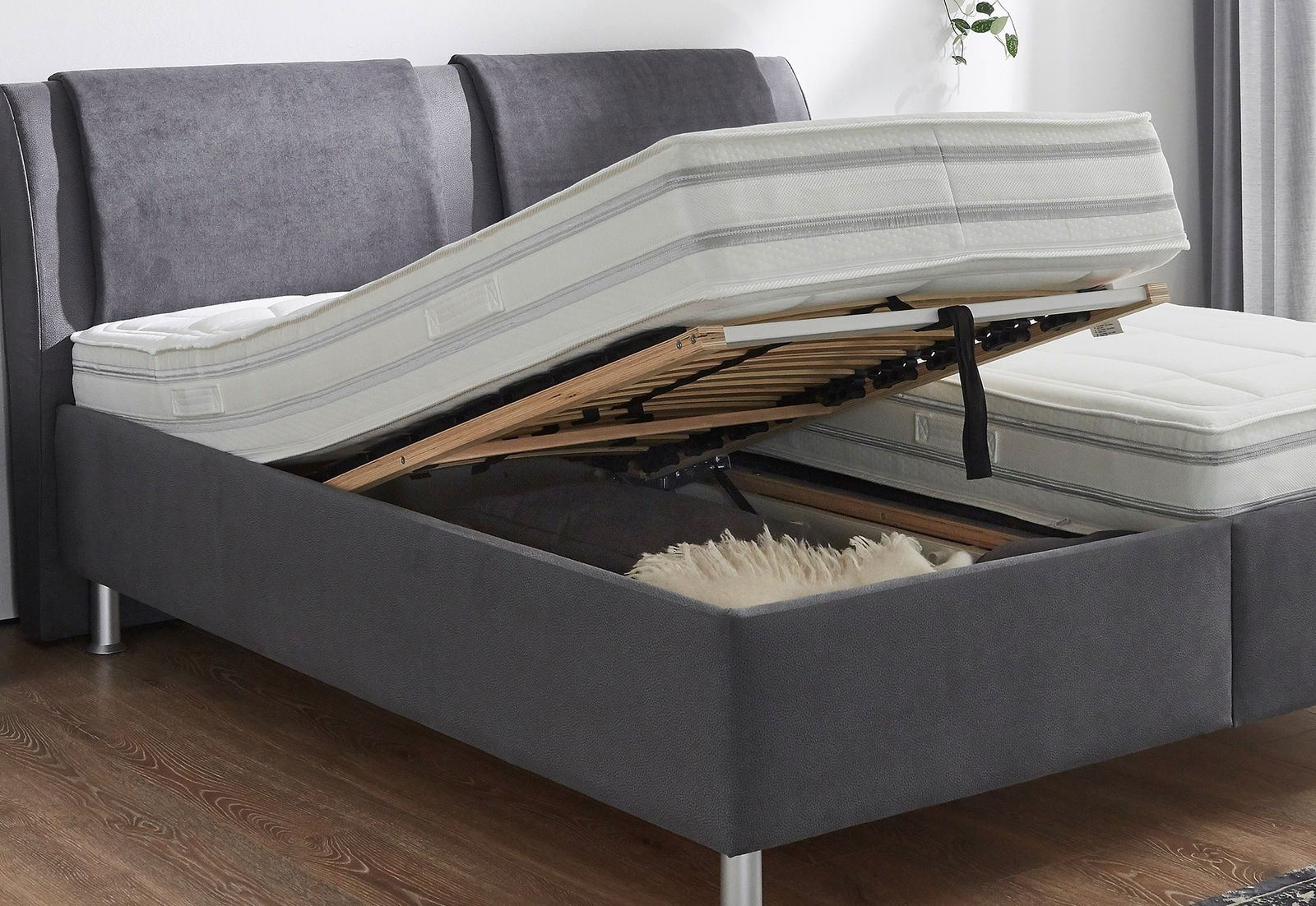 Polsterbett mit hochgeklappter Matratze und Lattenrost, seitliche Perspektive