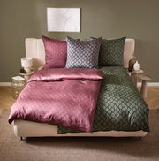 Wendebettwäsche in einem modernen Schlafzimmer, mit einer Seite in Rosa und der anderen in Grün, aus der Perspektive von vorne fotografiert.