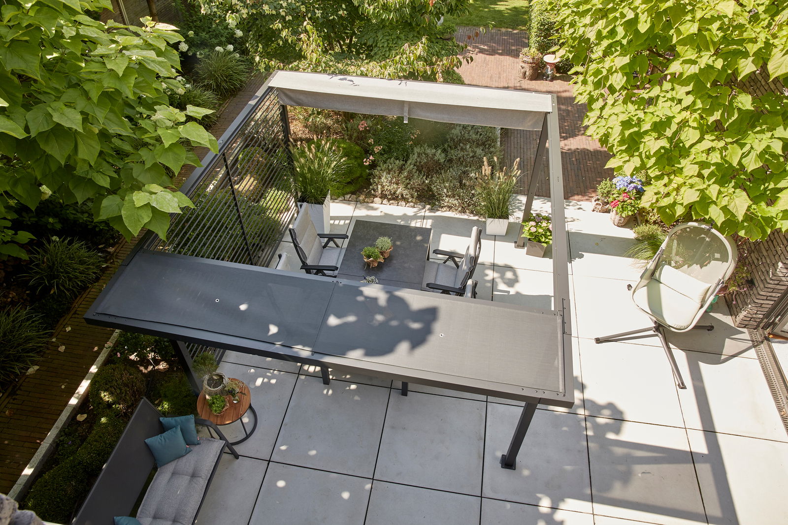 Blick von oben auf eine moderne Terrasse mit Pergola, Gartenmöbeln und üppiger Bepflanzung.