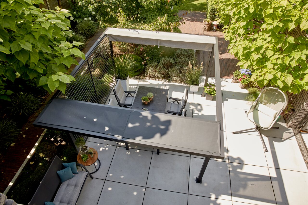 Bovenaanzicht van een modern terras met pergola, tuinmeubilair en weelderige beplanting.