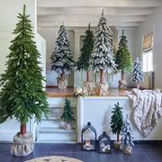 Verschiedene künstliche Tannenbäume in einem Raum, einige mit Schnee bedeckt, in unterschiedlichen Größen aufgestellt. Perspektive von vorne.