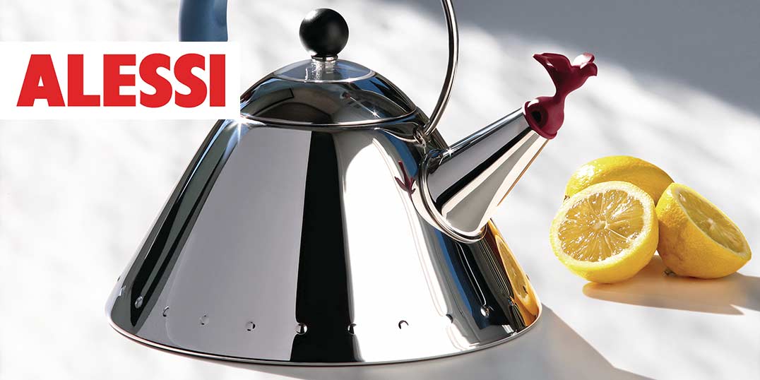 Glänzender Edelstahl-Wasserkocher von Alessi mit rotem, vogelförmigem Ausguss, begleitet von frischen Zitronenhälften auf einer glänzenden Oberfläche.