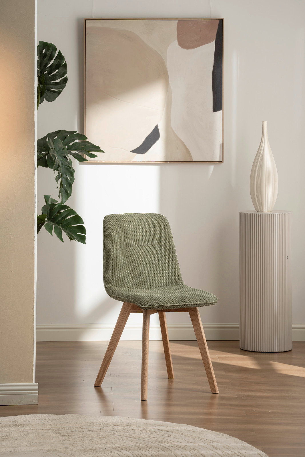 Moderner grüner Stuhl mit Holzbeinen, frontal fotografiert in einem stilvoll eingerichteten Raum mit Kunstwerk und Pflanze im Hintergrund.