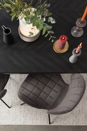 Draufsicht auf einen eleganten, gepolsterten Stuhl mit schwarzem Metallgestell, neben einem Tisch mit Kerzen und Pflanzen.