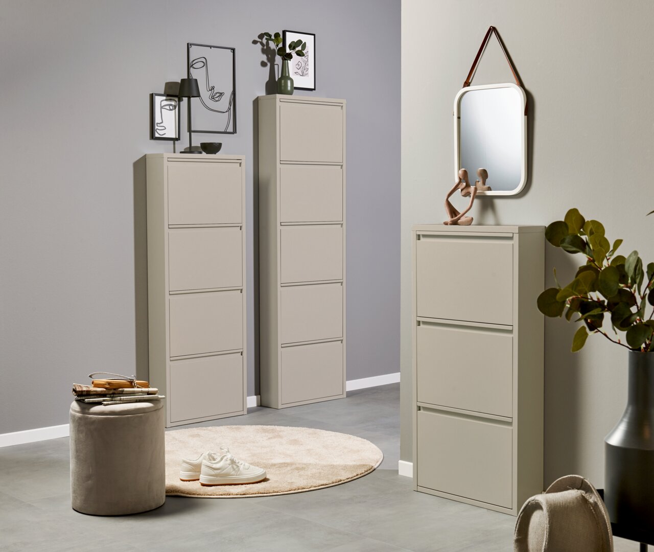Modernes, hellbeiges Schuhschrank-Set im Flur: zwei hohe, schmale Klappschränke und ein niedrigerer Klappschrank mit Spiegel darüber, fotografiert in leichter Schrägansicht von vorn.