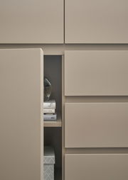 Nahaufnahme eines modernen, beigen Schranks mit offenen Türen, die Bücher und eine dekorative Schachtel zeigen.