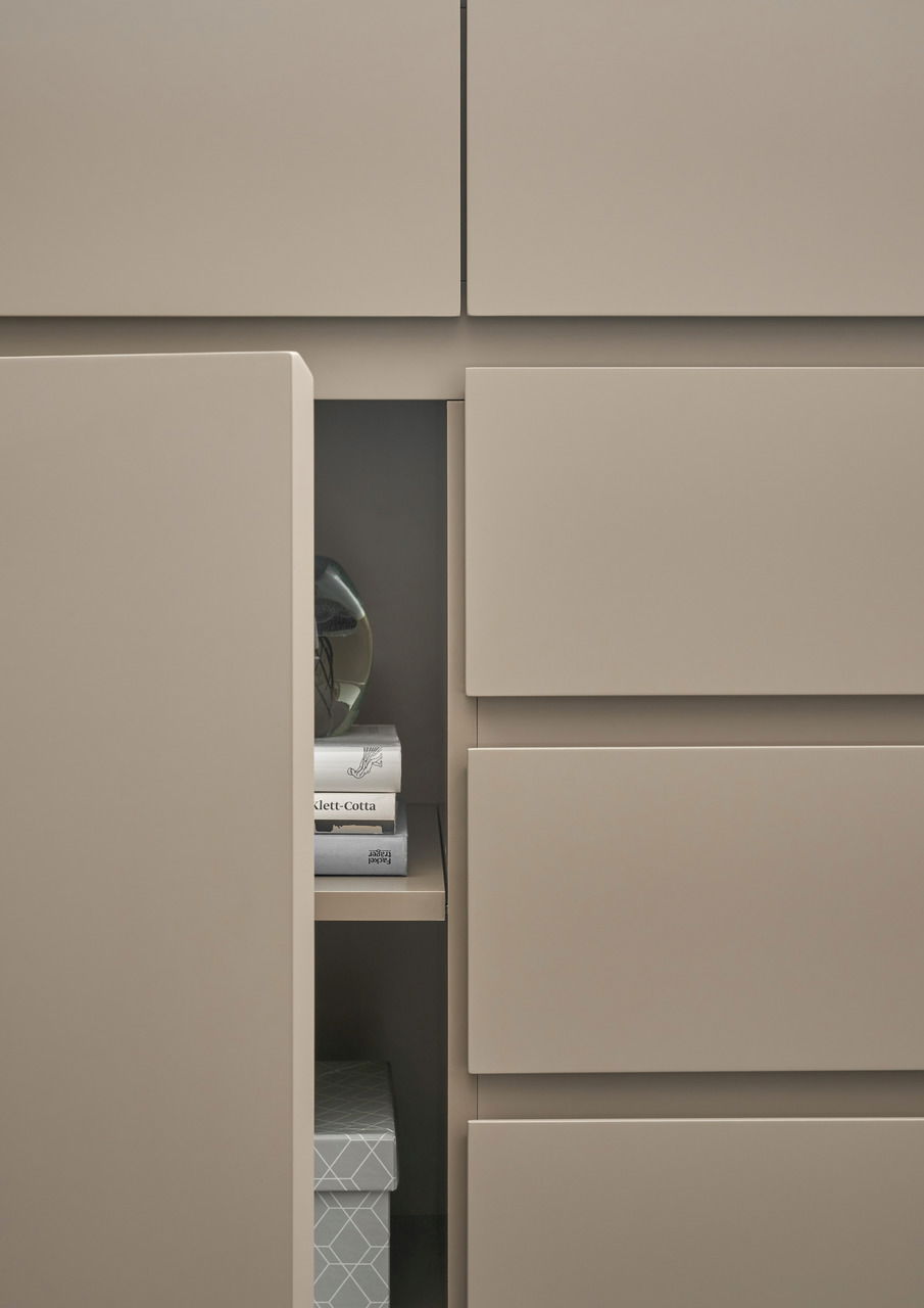 Nahaufnahme eines modernen, beigen Schranks mit offenen Türen, die Bücher und eine dekorative Schachtel zeigen.