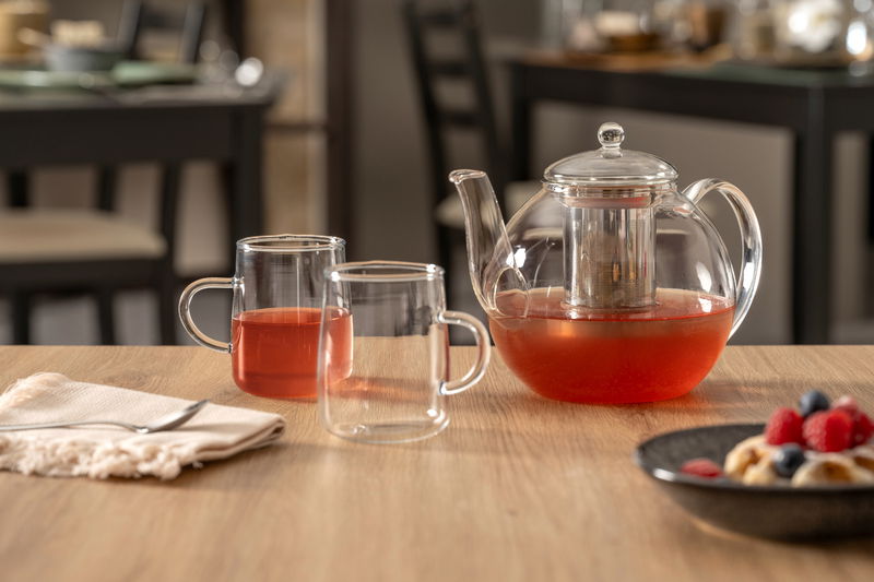 Leonardo Tee-Set 3-tlg. LIMITED EDITION Glas-Teekanne mit integriertem Sieb und zwei Glastassen, gefüllt mit rotem Tee, auf einem Holztisch. Perspektive: seitlich.