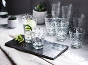 Ein Set von zwölf Gläsern mit optischem Design, präsentiert auf einem Tisch mit einer modernen und eleganten Perspektive.