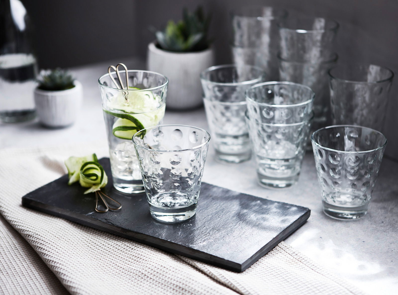 Ein Set von zwölf Gläsern mit optischem Design, präsentiert auf einem Tisch mit einer modernen und eleganten Perspektive.