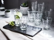 Ein Set von zwölf Gläsern mit optischem Design, präsentiert auf einem Tisch mit einer modernen und eleganten Perspektive.