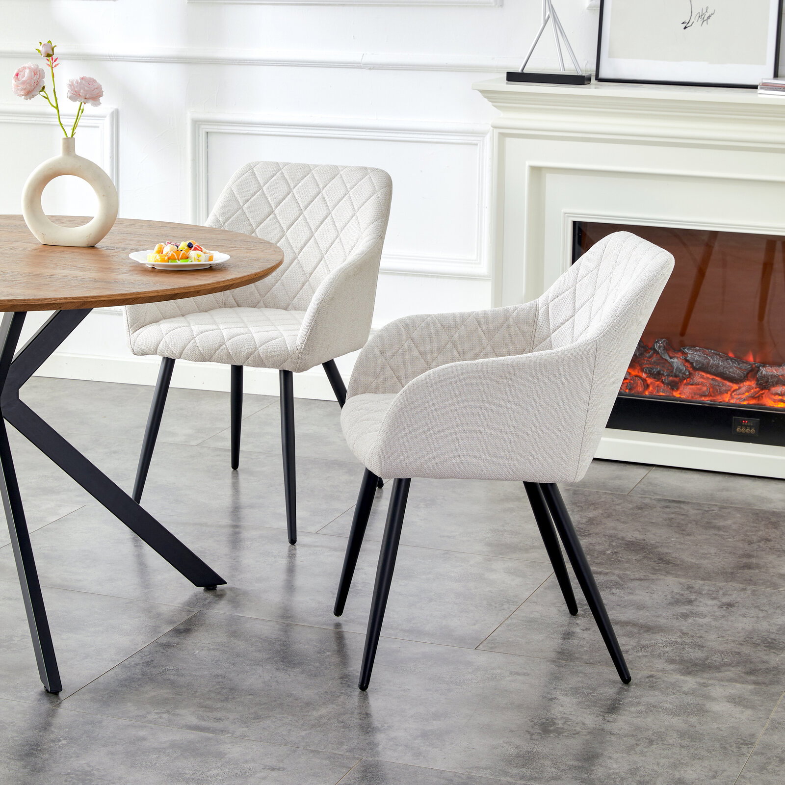 MID.YOU Stuhl 2er-Set LEA Zwei gepolsterte Esszimmerstühle in Creme mit Rautensteppung und schwarzen Metallbeinen an einem runden Holztisch, seitliche Perspektive im hellen Wohn-/Essbereich neben einem Kamin.