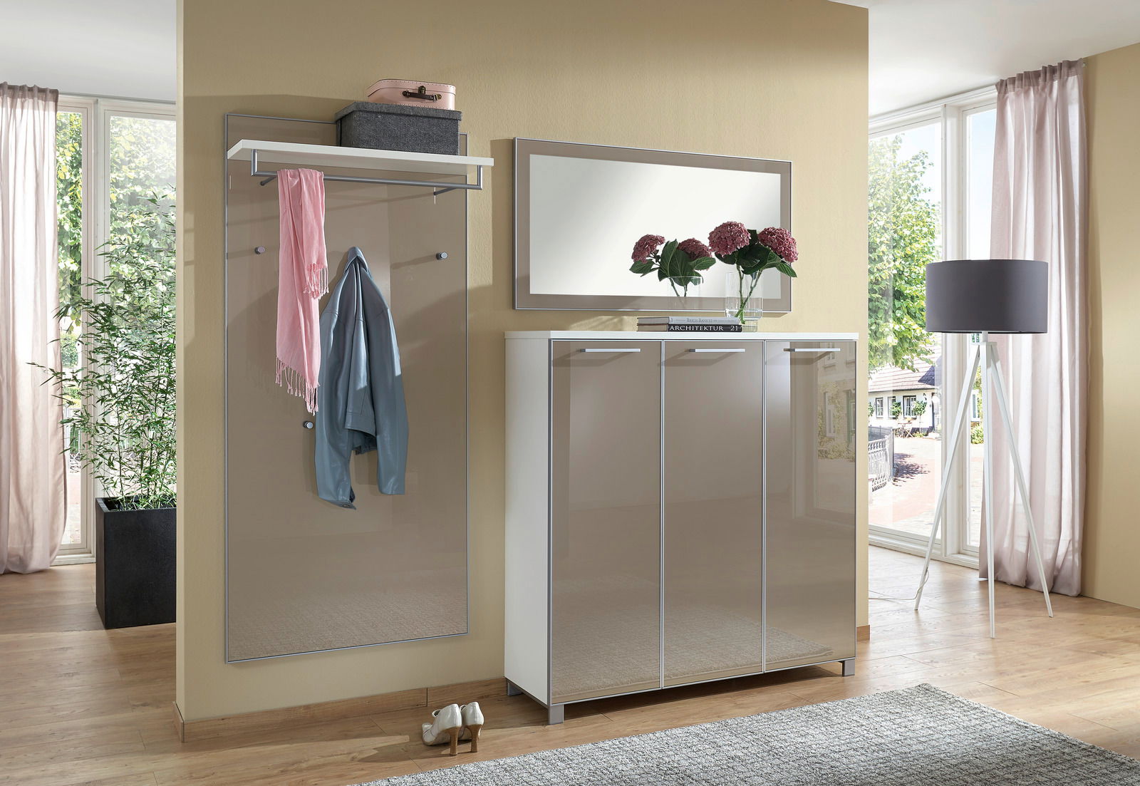 Modernes Garderoben-Set in einem hellen Raum mit großem Fenster, bestehend aus einem Spiegel, einer Garderobenleiste mit Ablage und einem dreitürigen Schrank. Perspektive von vorne.