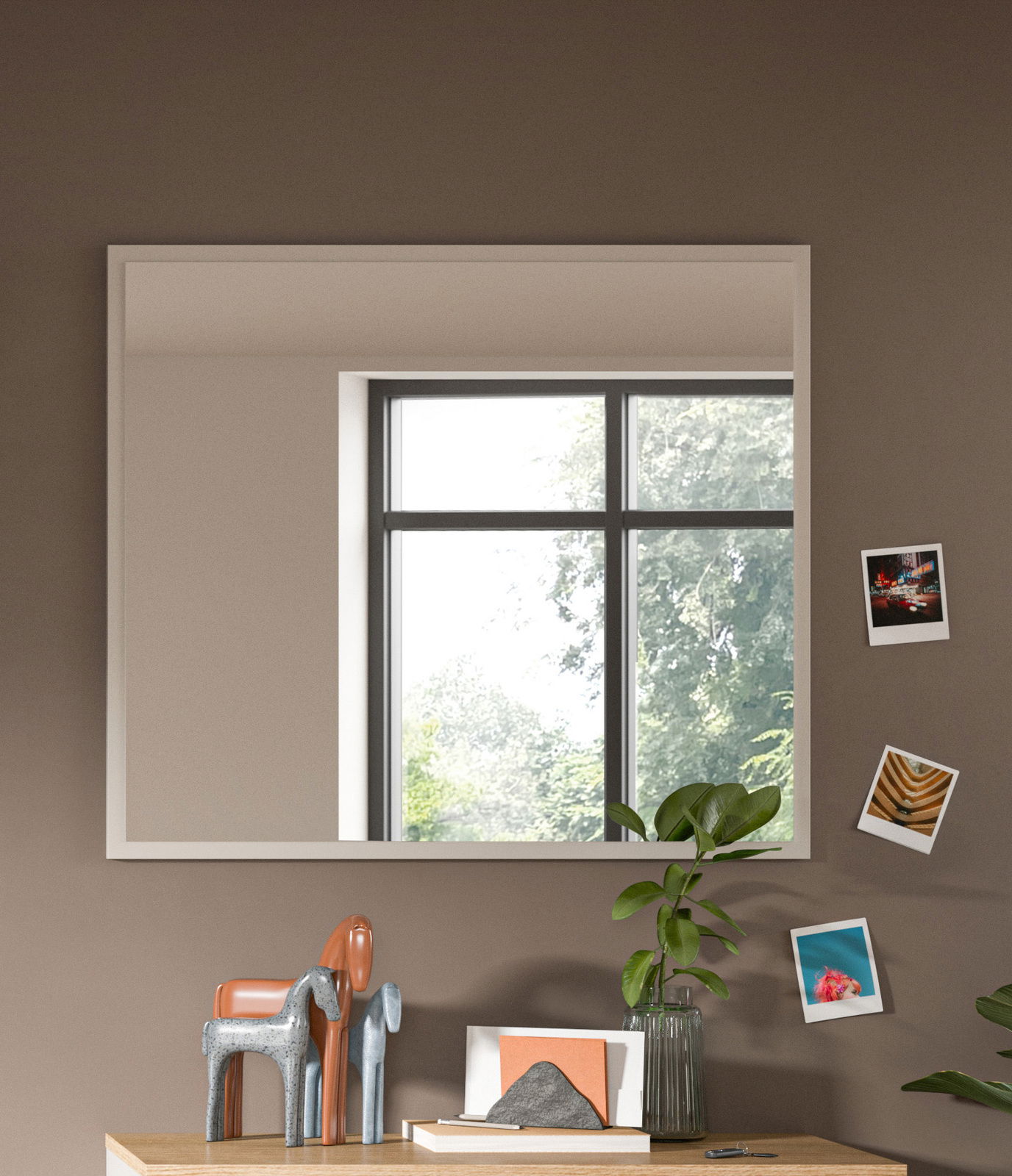 Moderner rechteckiger Spiegel an einer Wand, reflektiert ein Fenster mit Blick auf Bäume, dekoriert mit kleinen Fotos und Pflanzen, Perspektive von vorne.