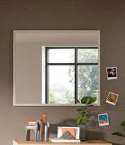 Moderner rechteckiger Spiegel an einer Wand, reflektiert ein Fenster mit Blick auf Bäume, dekoriert mit kleinen Fotos und Pflanzen, Perspektive von vorne.