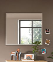 Moderner rechteckiger Spiegel an einer Wand, reflektiert ein Fenster mit Blick auf Bäume, dekoriert mit kleinen Fotos und Pflanzen, Perspektive von vorne.