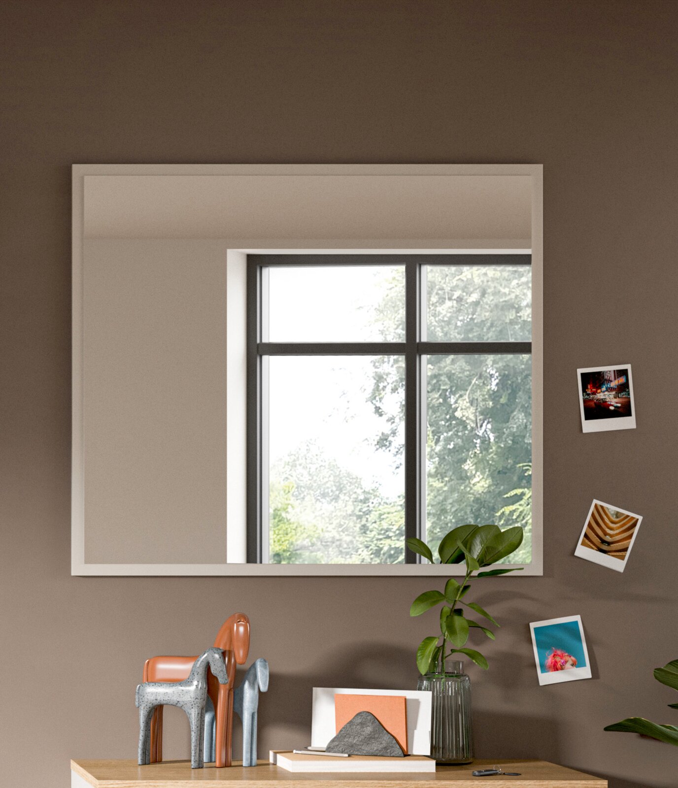 Moderner rechteckiger Spiegel an einer Wand, reflektiert ein Fenster mit Blick auf Bäume, dekoriert mit kleinen Fotos und Pflanzen, Perspektive von vorne.