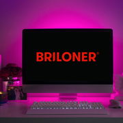 Ein Computerbildschirm mit dem Logo 'BRILONER' in roter Schrift, umgeben von einem pinken LED-Licht, das eine stimmungsvolle Beleuchtung erzeugt. Perspektive: Frontalansicht auf den Bildschirm und die beleuchtete Umgebung.