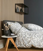 Bettwäsche-Set mit elegantem Paisley-Muster in Grau- und Beigetönen auf einem Bett, seitliche Perspektive, mit modernem Nachttisch und Dekoration.