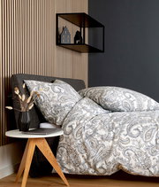 Bettwäsche-Set mit elegantem Paisley-Muster in Grau- und Beigetönen auf einem Bett, seitliche Perspektive, mit modernem Nachttisch und Dekoration.