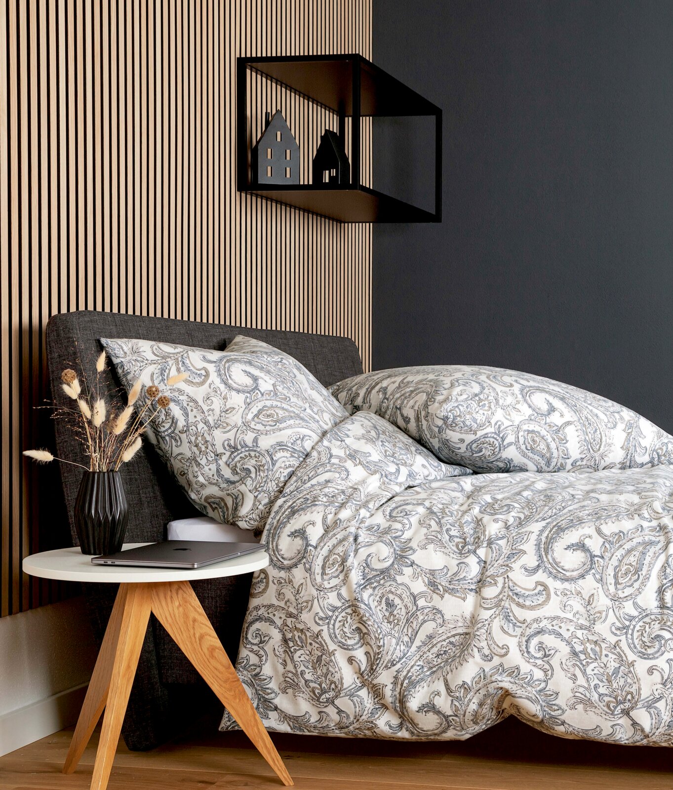 Beddengoedset met een elegant paisleypatroon in grijze en beige tinten op een bed, gezien vanuit de zijkant, met een modern nachtkastje en decoratie.